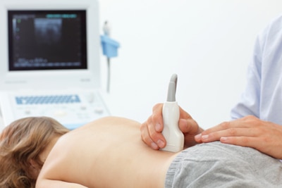 Una ecografía en un niño. Un técnico pasa una varita sobre la parte baja de la espalda de un niño, que envía una imagen a la pantalla de una computadora.