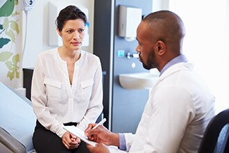 A woman sits on an examining table and talks to a health care professional.