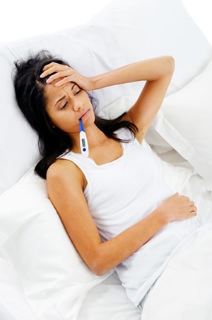 Mujer acostada en la cama, tomándose la temperatura con un termómetro.