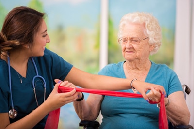 Older woman in a wheelchair working with resistance bands with help from a health care professional.