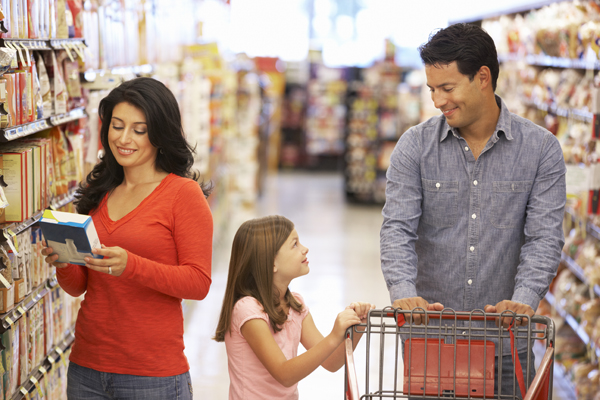 Una mujer que está leyendo los envases de los alimentos en un supermercado con su familia.