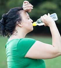 Una mujer tomando agua después de sudar por hacer ejercicio.