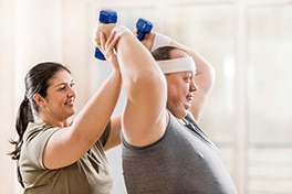 A man lifting weights with a woman providing support