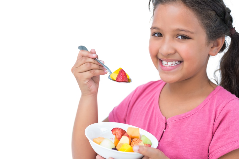 Niña sonriente comiendo un plato de ensalada de frutas.