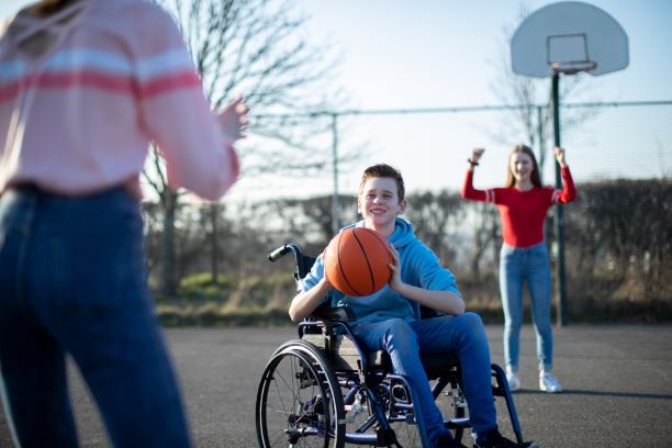 A teenage boy in a wheelchair plays basketball with friends.