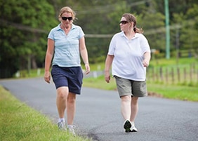 Two women walking down a paved road with earbuds in their ears.