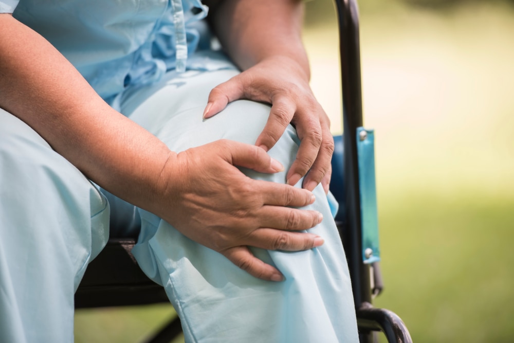 Person sitting in a wheelchair and holding one knee with both hands.