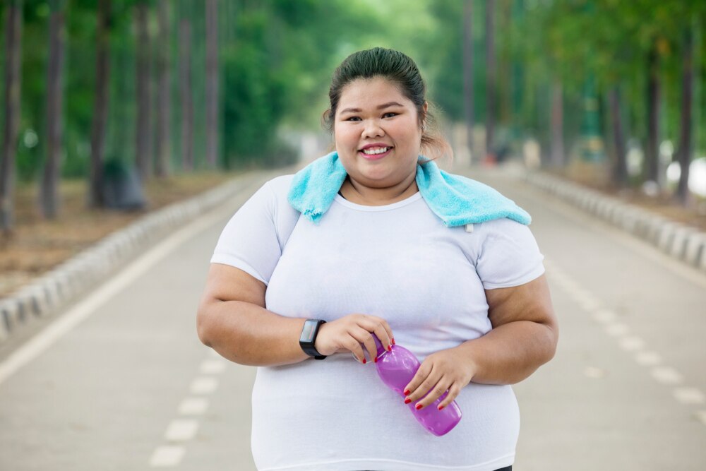 A woman walks down a street holding a water bottle and wearing a fitness tracker.