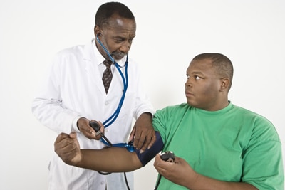 Un médico revisando la presión arterial de un hombre que tiene obesidad.