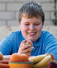 Overweight boy with bowl of fruit.