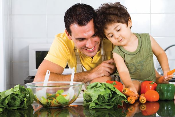Un padre y su hijo pequeño preparan una ensalada con pimientos, zanahorias y lechuga. 