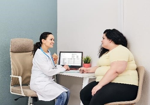 A health care professional talks in her office with a young woman who has obesity.