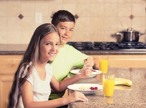 صورة لصبي وفتاة يجلسان على طاولة المطبخ يأكل الفطور