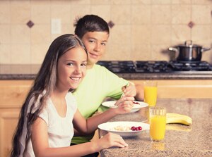 Photo of boy and girl sitting at kitchen counter eating breakfast