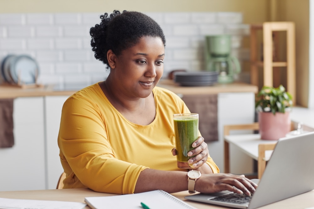 A woman using a laptop and drinking a smoothie.