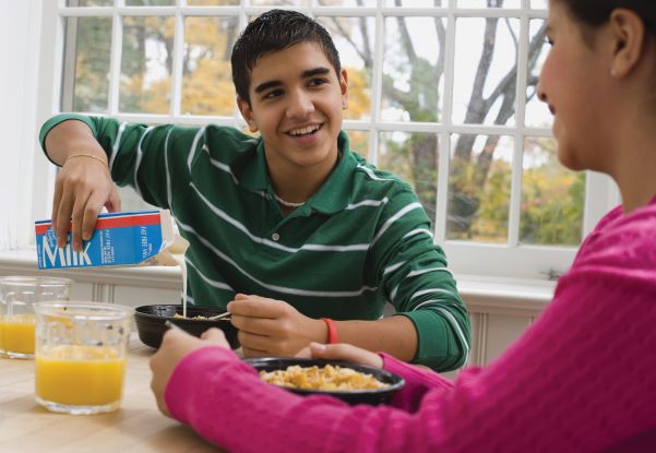 Teen boy and his mother eat a breakfast of whole-grain cereal, low-fat milk, and fresh fruit juice.