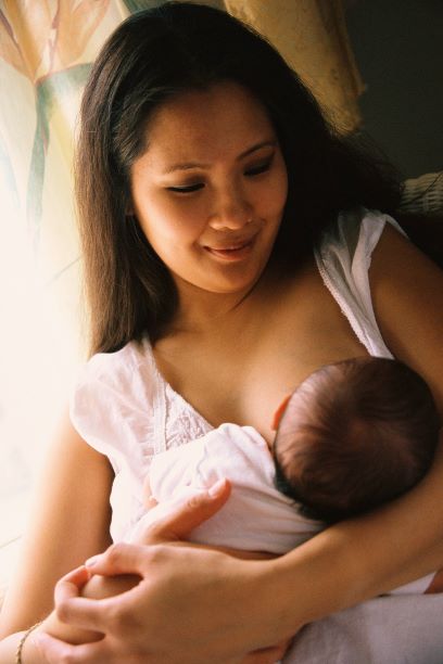 A young mother nurses her baby at her breast.