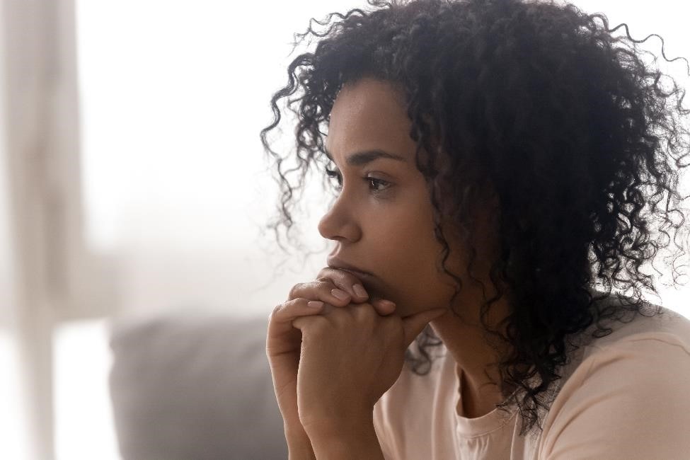 A young woman sits with her hands against her chin, lost in her thoughts.