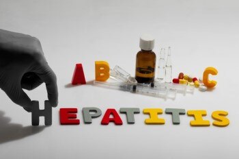Cut-out letters spelling “hepatitis” with medicine in the background.