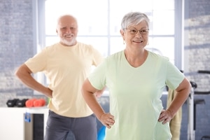 An exercise class, with an older woman in the foreground and an older man in the background.