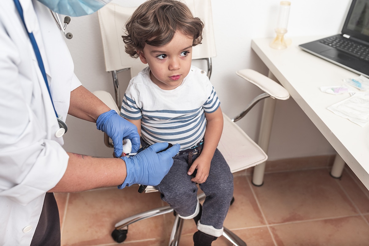 Pediatrician takes blood sample from toddler to check blood glucose.