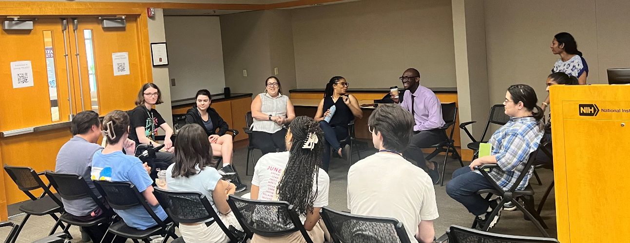 A group of fellows sitting in chairs in a circle.