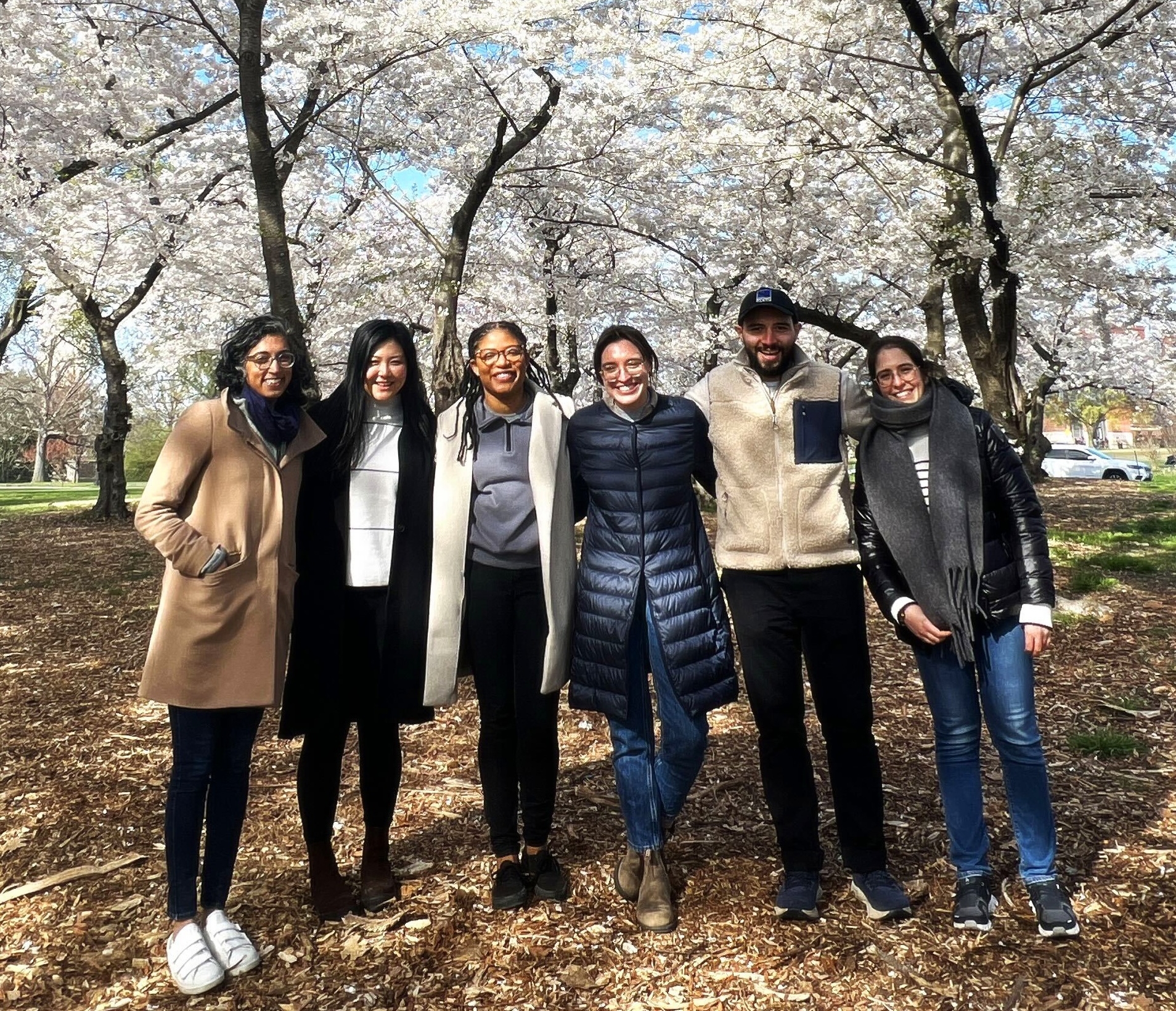 Lab members standing and smiling outside with flowering trees in the background.