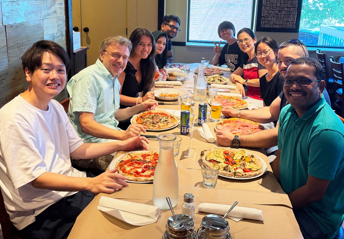 Members of the Wess lab smiling and sitting at a long table with plates of food in front of them.