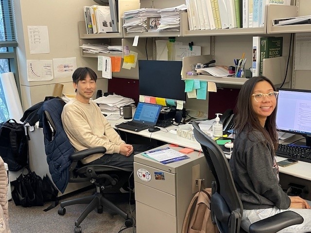 Juhyun Kim and Nicole Nguyen sitting at their desks in front of their computers and smiling.