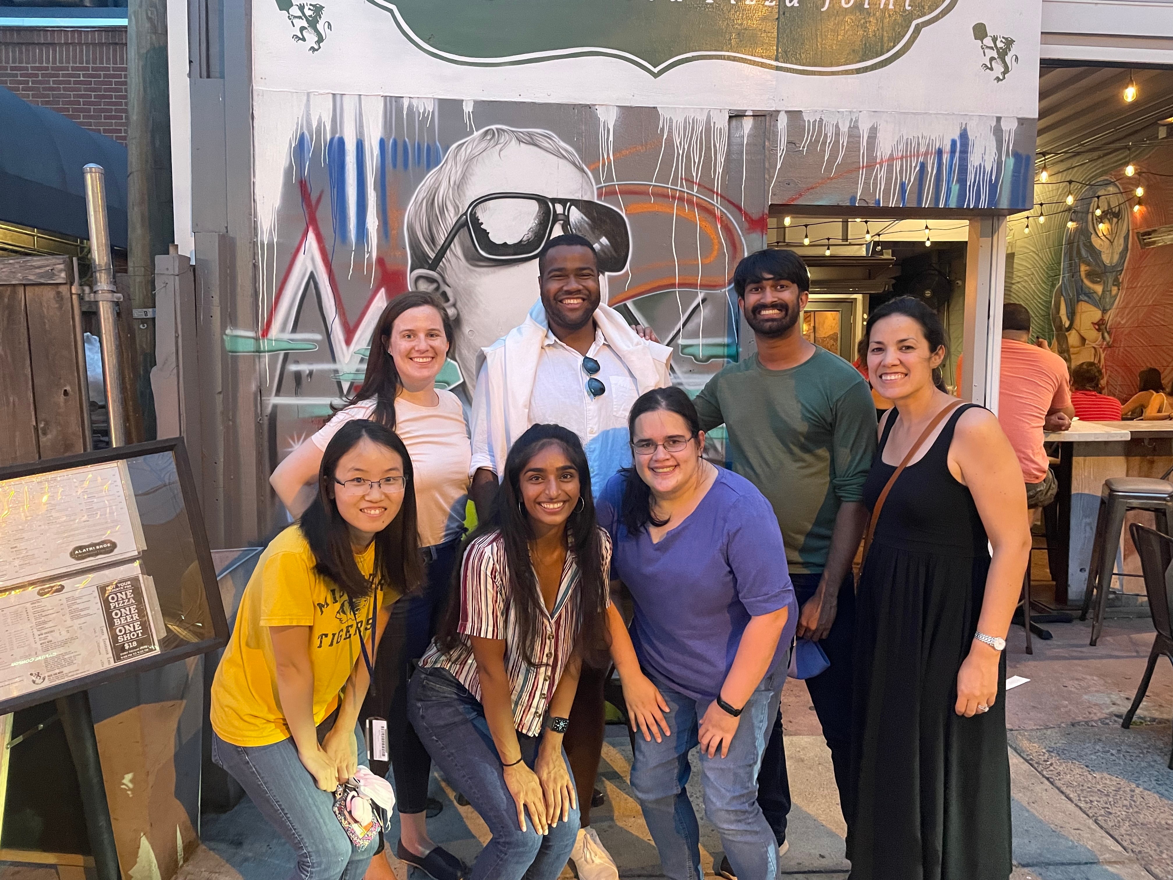 Photo of the lab members of the Section of Regulatory RNAs smiling in front of a mural.