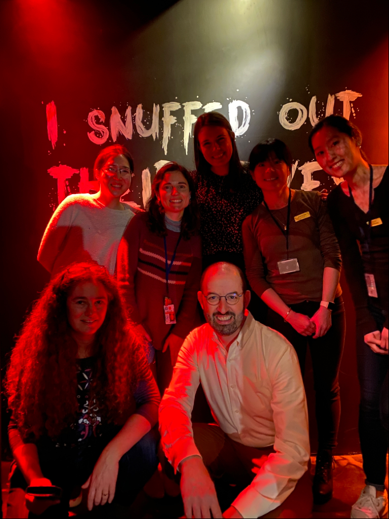 Group photo in a dark room, in front of sign saying I SNUFFED OUT