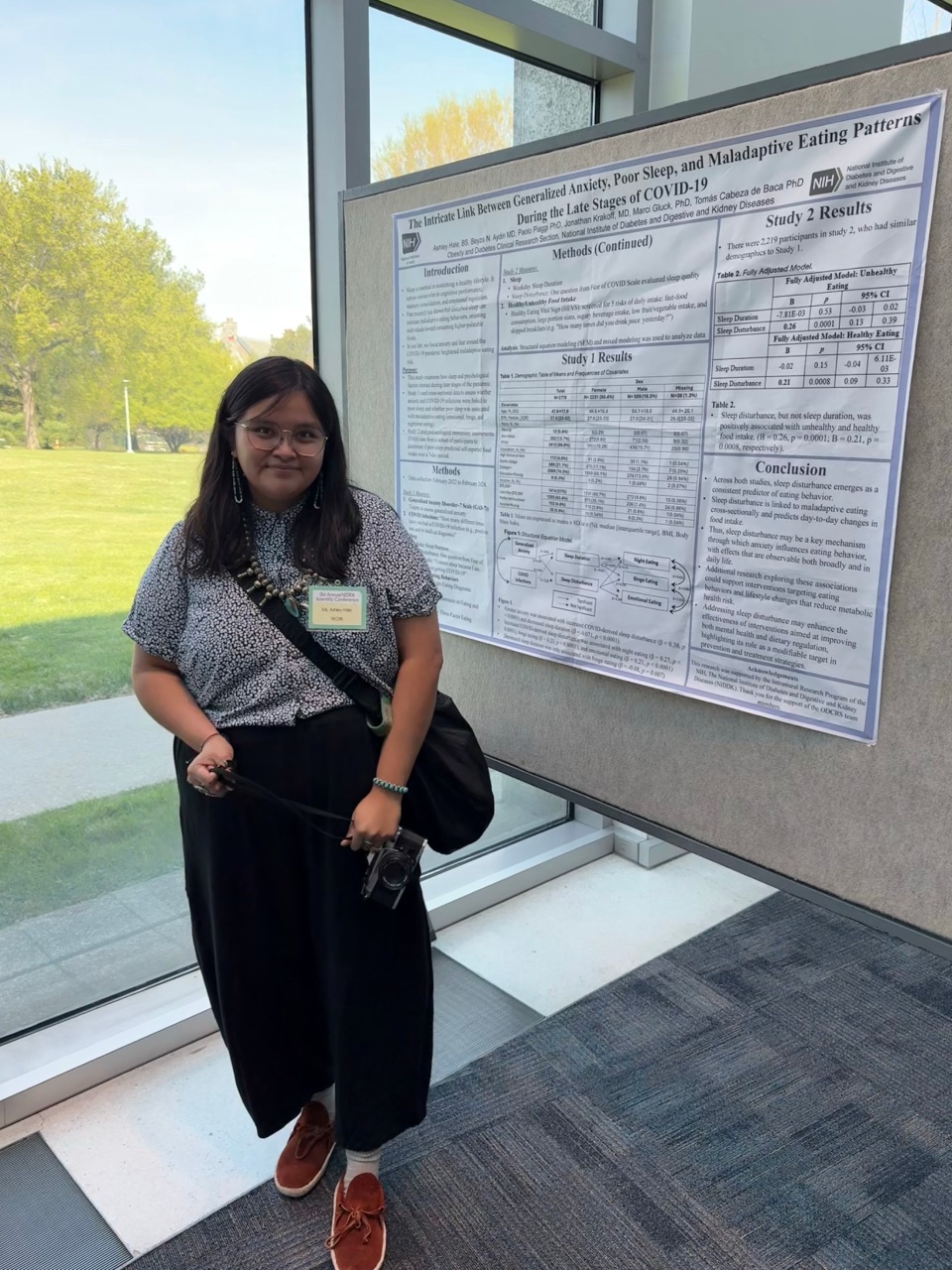 IRTA Fellow Ashley Hale stands in front of a poster titled "The Intricate Link Between Generalized Anxiety, Poor Sleep, and Maladaptive Eating Patterns During the Late Stages of COVID-19"