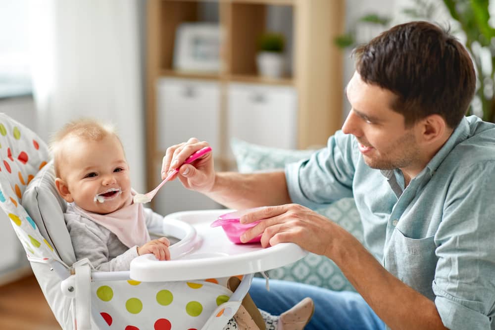 An adult male feeds food to an infant child with a spoon.