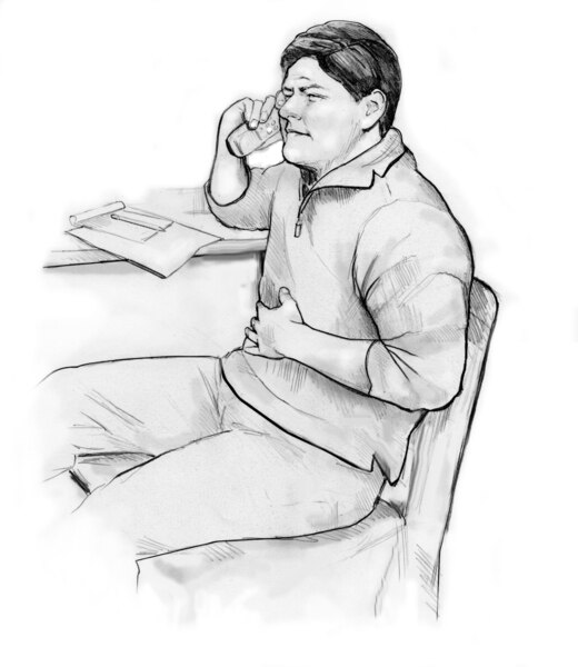 A seated man using the telephone while holding his hand to his abdomen.
