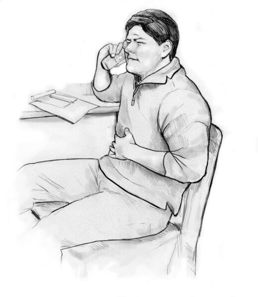 A seated man using the telephone while holding his hand to his abdomen.