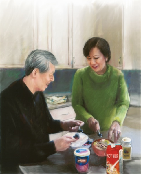 A man eating yogurt and a woman eating cereal in a kitchen. A container of yogurt, a carton of soy milk, and a bottle of lactase enzyme tablets are on the table.