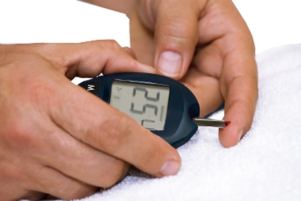 Photograph of two hands holding a blood glucose meter. A test strip extends from the meter to one index finger. A drop of blood has been applied to the end of the test strip. The screen on the meter that shows results says 254.