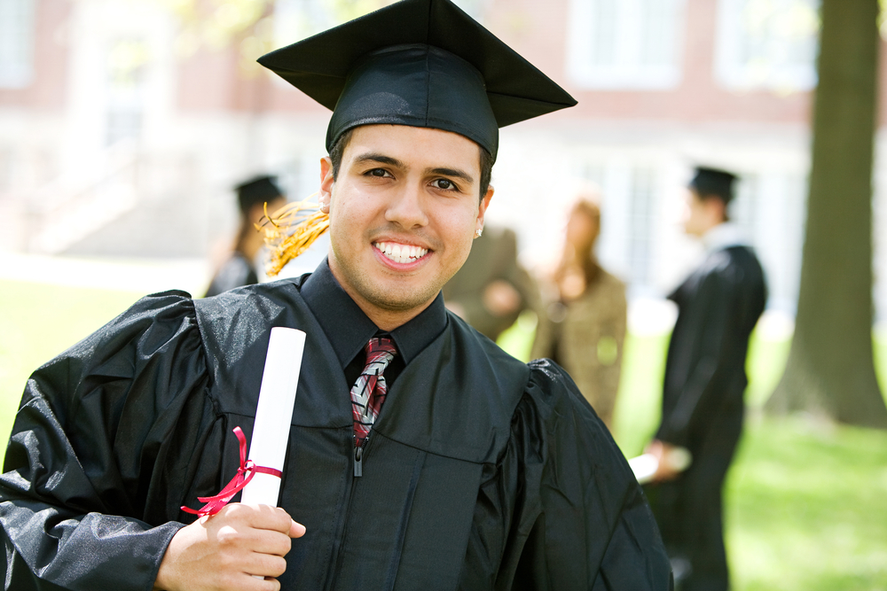 Un adulto joven con toga y birrete de graduación, sonriendo con un diploma en la mano.