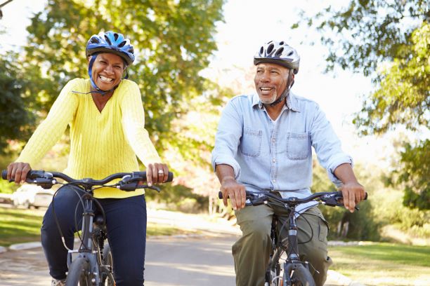 An older couple biking in the countryside, wearing helmets.