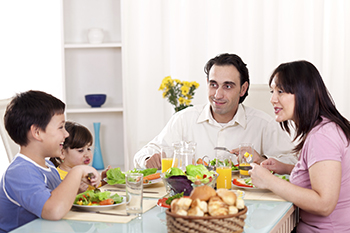 Una familia que está sentada alrededor de una mesa comiendo una comida saludable.