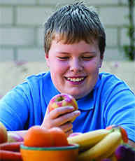 Overweight boy with bowl of fruit.
