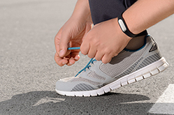 A person tying their running shoes while wearing a fitness tracker band